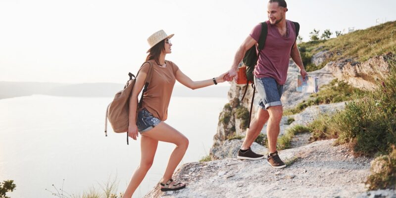 Two tourist with backpacks climb to the top of the mountain and enjoying sunrise.